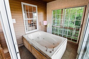 A bathroom with a large bathtub, wooden walls, a window with a view of trees, and a towel rack.