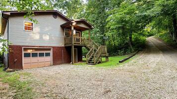 A two-story house with a garage, a wooden deck, and a gravel driveway.