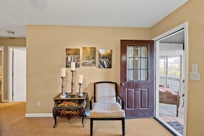 A room with a wooden door, a chair, a small table with candles, and three framed pictures on the wall.