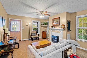 Un salón con chimenea, ventilador de techo y vistas al exterior.