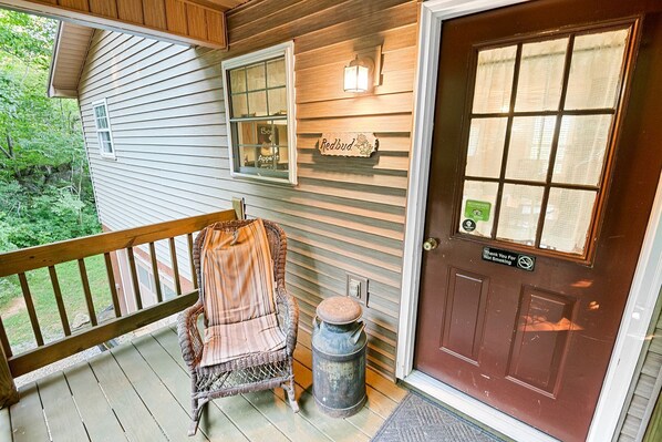 A wooden porch with a wicker chair, a small trash can, and a door with a 'Not Smoking' sign.