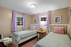 Une chambre avec deux lits simples, une table de chevet avec une lampe et une fenêtre avec des rideaux.