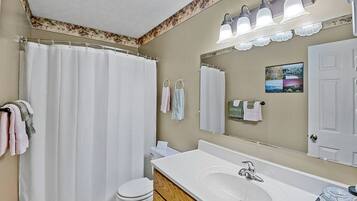 A bathroom with a shower curtain, a toilet, a sink with a mirror, and towels on hooks.