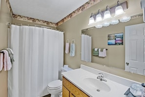 A bathroom with a shower curtain, a toilet, a sink with a mirror, and towels on hooks. - Fully Furnished Camping Cabin near Cherokee National Forest (Greeneville)