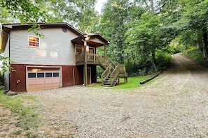Une maison à deux étages avec un garage, une terrasse en bois et une allée gravillonnée.
