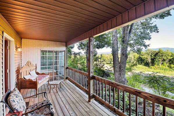 A wooden deck with a bed and chairs, overlooking a natural landscape.