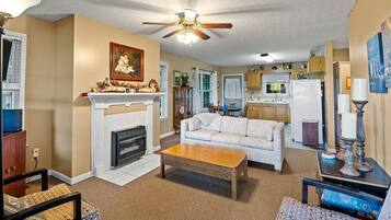 A living room with a fireplace, sofa, coffee table, and a ceiling fan.