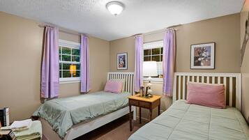 A bedroom with two single beds, a bedside table with a lamp, and a window with curtains.