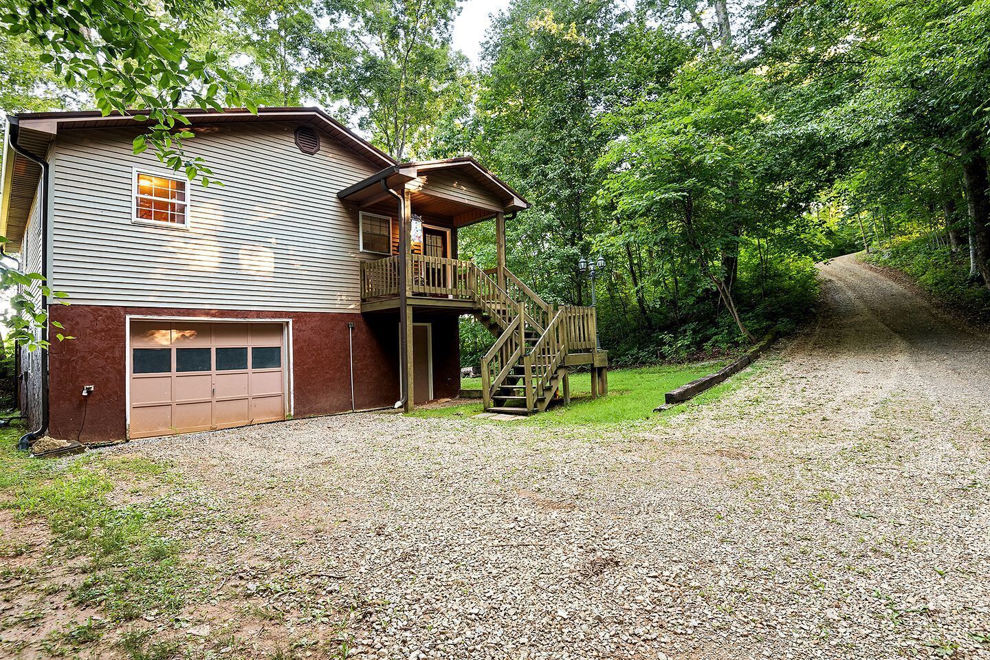 A two-story house with a garage, a wooden deck, and a gravel driveway.