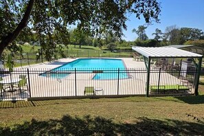 A fenced backyard with a swimming pool, a covered seating area, and a grassy lawn.