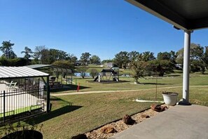 A covered outdoor area with a playground, a fenced area, and a body of water in the background.