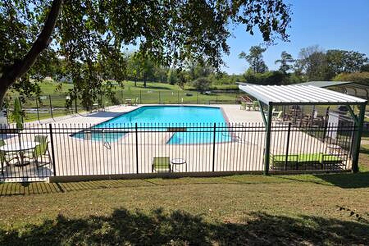 Une cour arrière clôturée avec une piscine, un espace salon couvert et une pelouse.