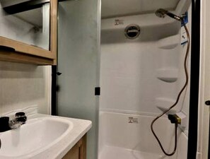 A bathroom with a sink, mirror, and shower enclosure.