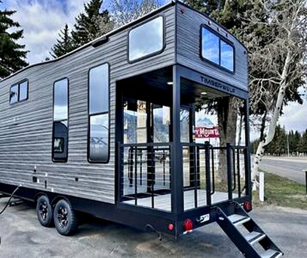 A modern RV with a covered front area, large windows, and a ramp for access.