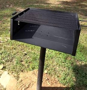 A black outdoor grill with a flat top and a side compartment, mounted on a metal stand.