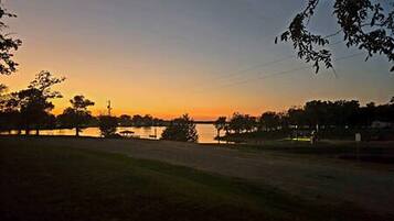 Een zonsondergang boven een wateroppervlak, met bomen en een hek op de voorgrond.