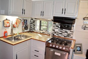 A compact kitchen with white cabinets, a stainless steel sink, a stove, and a window with a view.