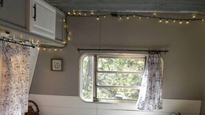 A cozy RV bedroom with a bed, a window, and string lights. - Texas Hill Country Vintage Caravan Glamping (Marble Falls)
