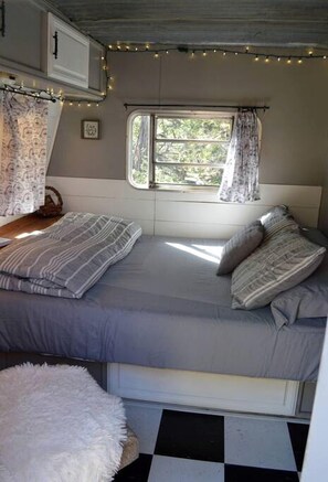 Un dormitorio acogedor en una casa rodante, con cama, ventana y luces colgantes.