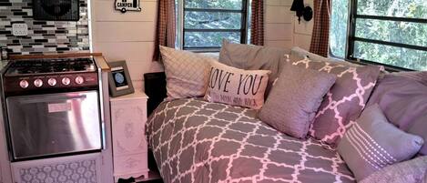 A cozy RV interior with a kitchenette, a bed with patterned bedding, and a window with curtains.