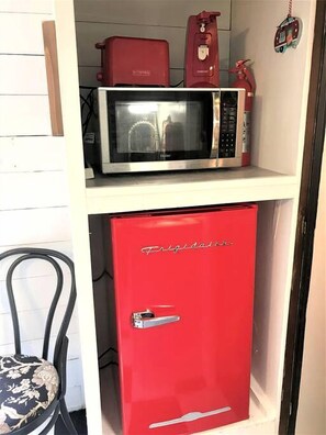 A compact kitchenette with a microwave and a red refrigerator.