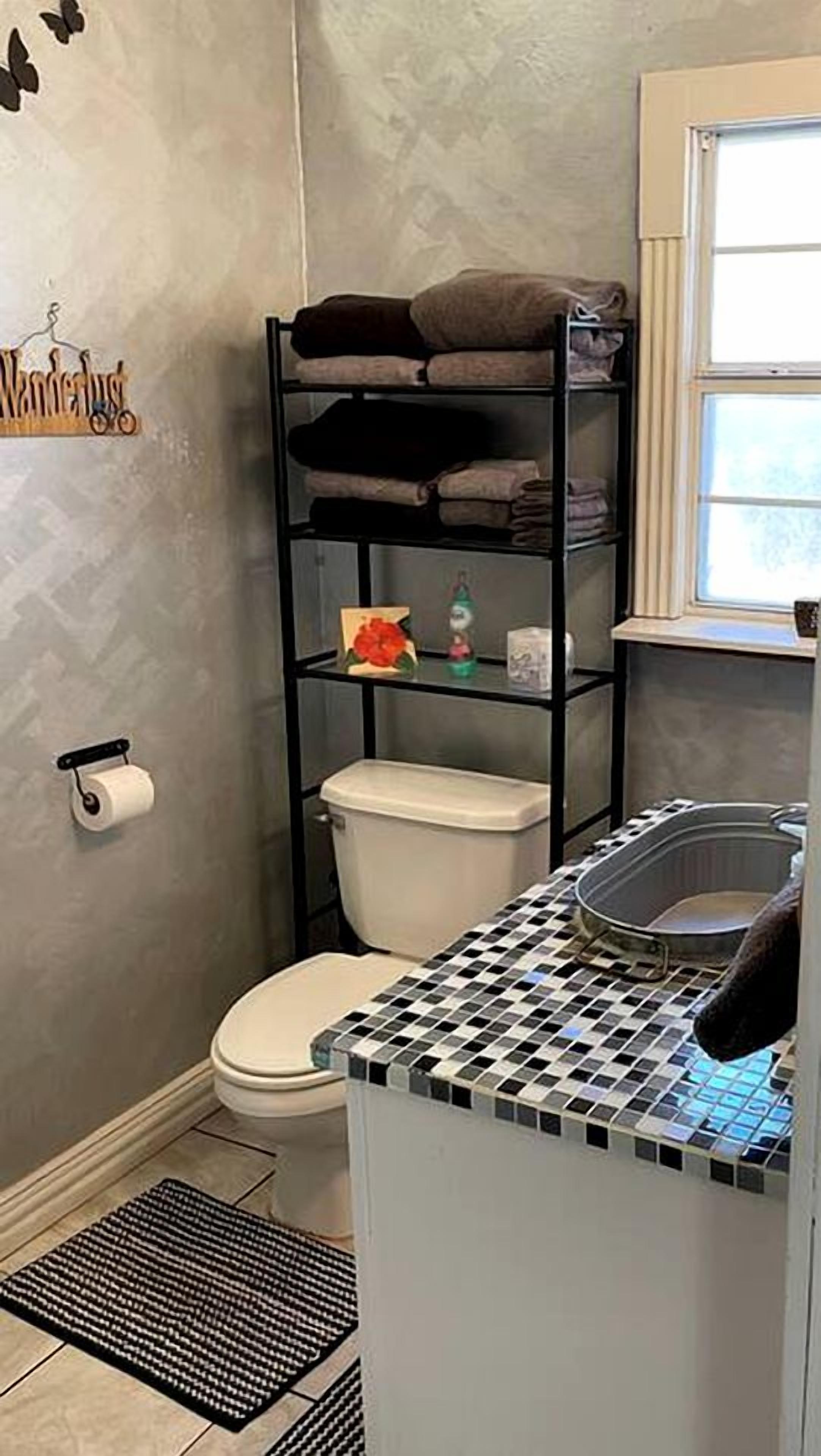 A bathroom with a toilet, a shelf with towels, a toilet paper holder, and a small shelf with toiletries.