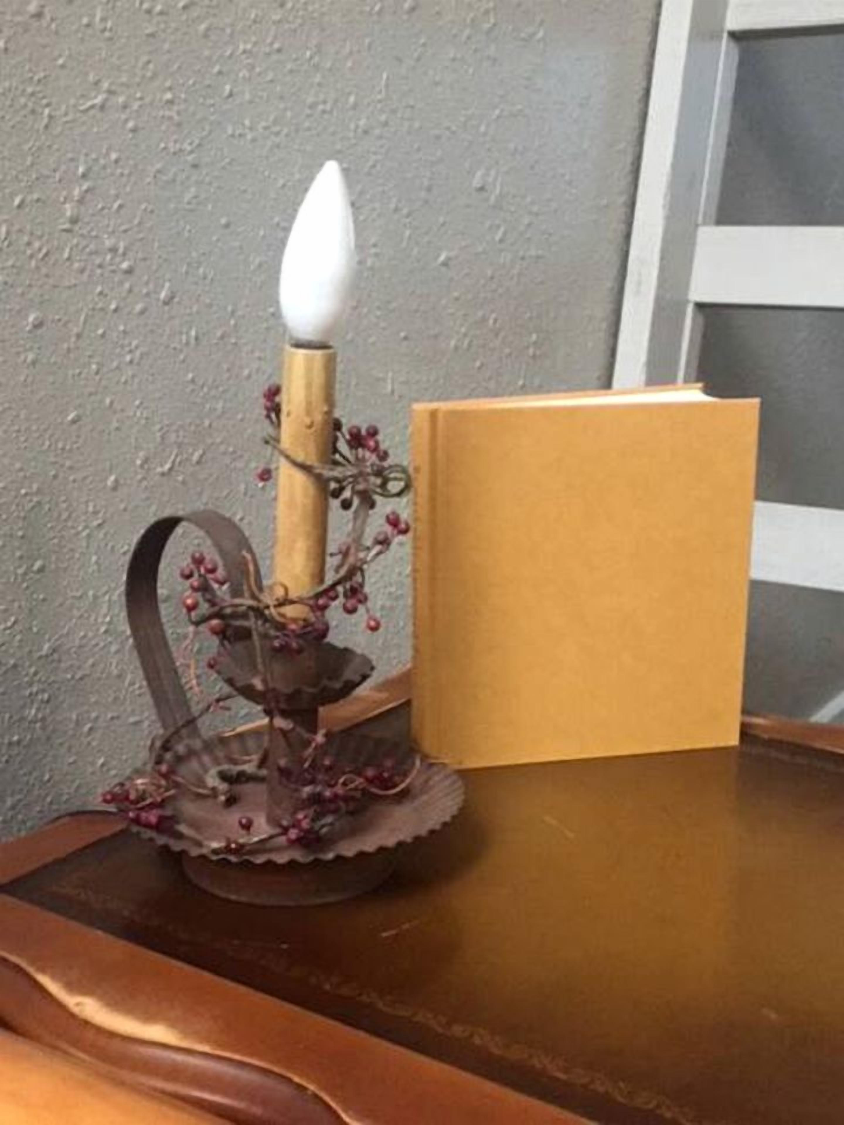 A candle holder with a lit candle, a book, and a decorative branch on a wooden surface.