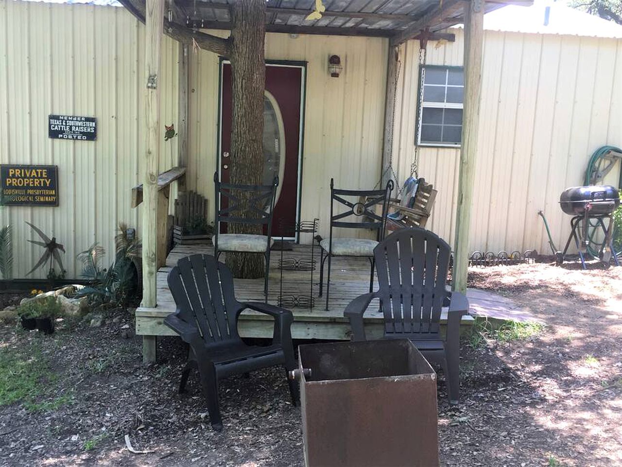Un porche abrité avec deux chaises et une table, une porte rouge et une boîte aux lettres indiquant qu’il s’agit d’une propriété privée.
