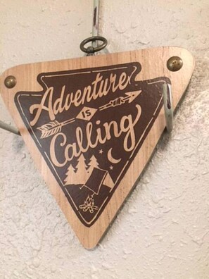 A wooden sign with the text 'Adventure Calling' and symbols of a compass, trees, and a tent. - Lovely Studio Rental with Hamilton Creek Views for Vacation in Marble Falls, Texas (Marble Falls)