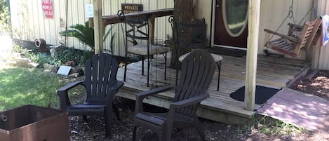 A porch with Adirondack chairs, a wooden table, and a swing chair.