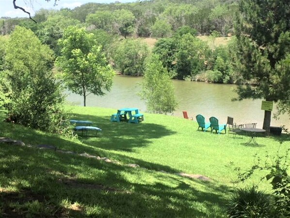 A grassy area with picnic tables and chairs near a lake.