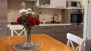 Une table de salle à manger en bois sur laquelle est posé un vase transparent rempli de fleurs rouges et blanches.