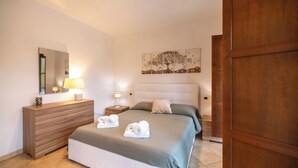 Une chambre d’hôtel comprenant un lit, une commode en bois, un miroir, une table de chevet et une œuvre d’art murale.