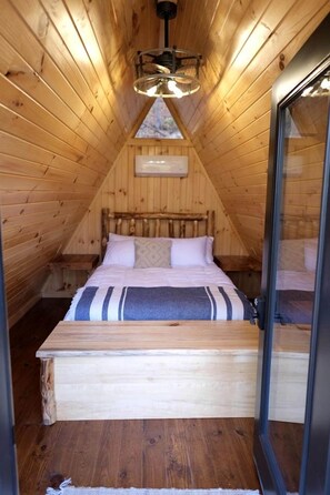 A cozy attic bedroom with a wooden sloped ceiling, a bed with a striped blanket, and a skylight. - Two Person A-frame near Tappan Lake, Ideal to Reconnect with Nature in Ohio (Deersville)