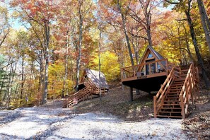 Eine Holzjagdhaushälfte mit Treppe und einer Veranda, umgeben von Bäumen in Herbstfarben.