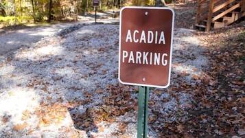 A sign for Acadia parking in a forested area with gravel paths and a wooden bridge.