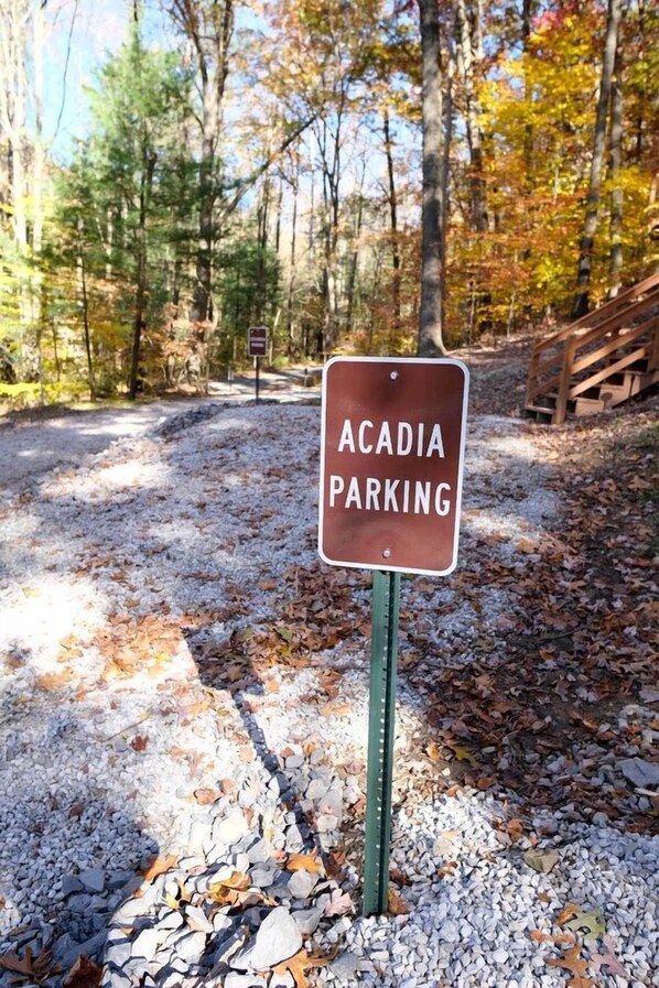 Señal de estacionamiento Acadia en zona boscosa con senderos de grava y un puente de madera.