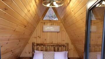 A cozy attic bedroom with a wooden sloped ceiling, a bed with a striped blanket, and a skylight.