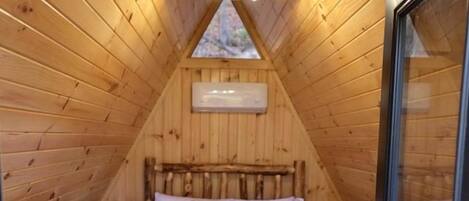 A cozy attic bedroom with a wooden sloped ceiling, a bed with a striped blanket, and a skylight.