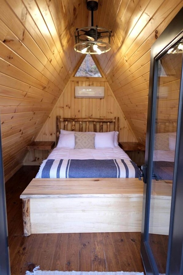 A cozy attic bedroom with a wooden sloped ceiling, a bed with a striped blanket, and a skylight.