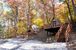 A wooden cabin with a staircase and a deck, surrounded by autumn-colored trees.
