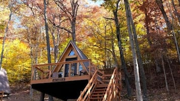 Una cabaña con escalera de madera y terraza, rodeada de árboles de colores otoñales.