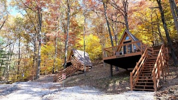 A wooden cabin with a staircase and a deck, surrounded by autumn-colored trees.