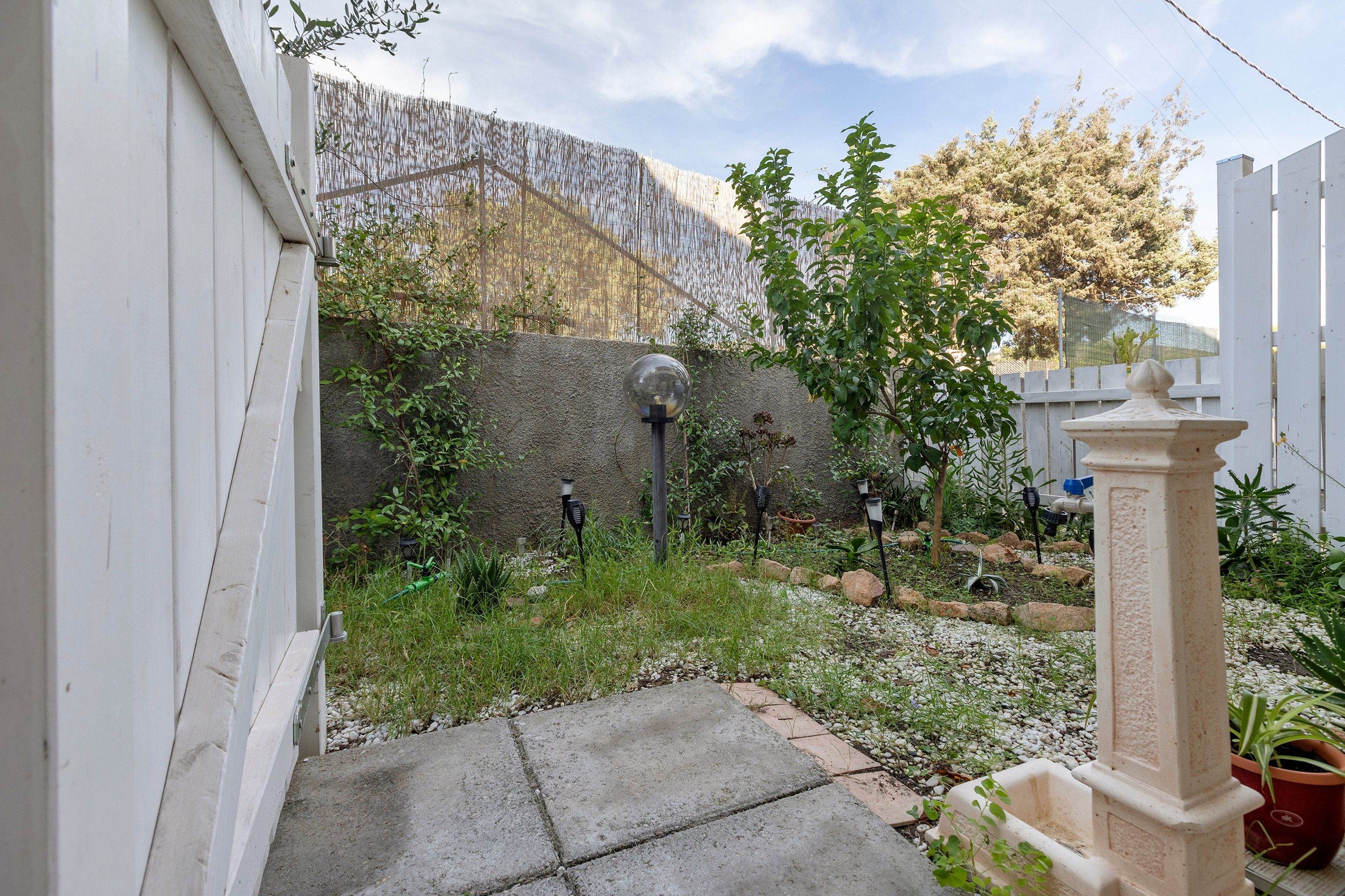 Ein Garten mit einem Kiesweg, einem weißen Zaun und verschiedenen Pflanzen.