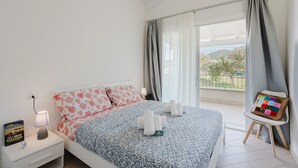 A bedroom with a bed, a nightstand, a chair, and a view of the outdoors. - Casa Lidia with Shared Pool, Private Parking, and Garden; Bouganville Residence in Viddalba (Viddalba)