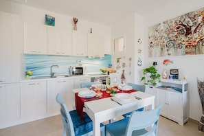 Una cocina moderna con armarios blancos, salpicadero azul y una zona de comedor con mesa blanca y sillas azules.