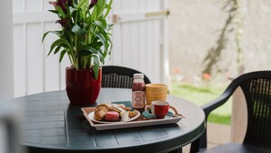 A round table with a tray of pastries, a red potted plant, a bottle, and a mug. - Casa Lidia with Shared Pool, Private Parking, and Garden; Bouganville Residence in Viddalba (Viddalba)
