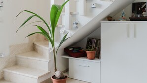 A staircase with a potted plant, a white cabinet with a red cushion, and a small shelf with decorative items. - Casa Lidia with Shared Pool, Private Parking, and Garden; Bouganville Residence in Viddalba (Viddalba)