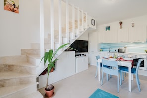 Una cocina moderna con armarios blancos, una zona de comedor con sillas azules y una escalera con barandillas blancas.