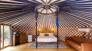 A yurt interior with a bed, a sofa, a chest of drawers, and a small table. - Peaceful Romantic Yurt with Hot Tub in Wimberley, Texas (Wimberley)